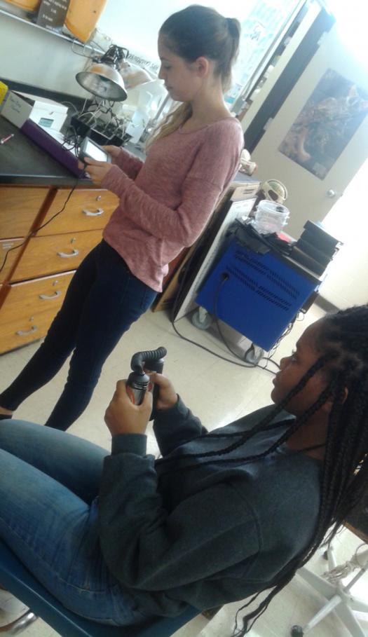 An 11th grade IB Biology student works after school on her science fair project, testing the effect of body position on heart rate. She uses Labquest 2 to calculate an average heart rate. The seated student is holding a heart rate sensor.