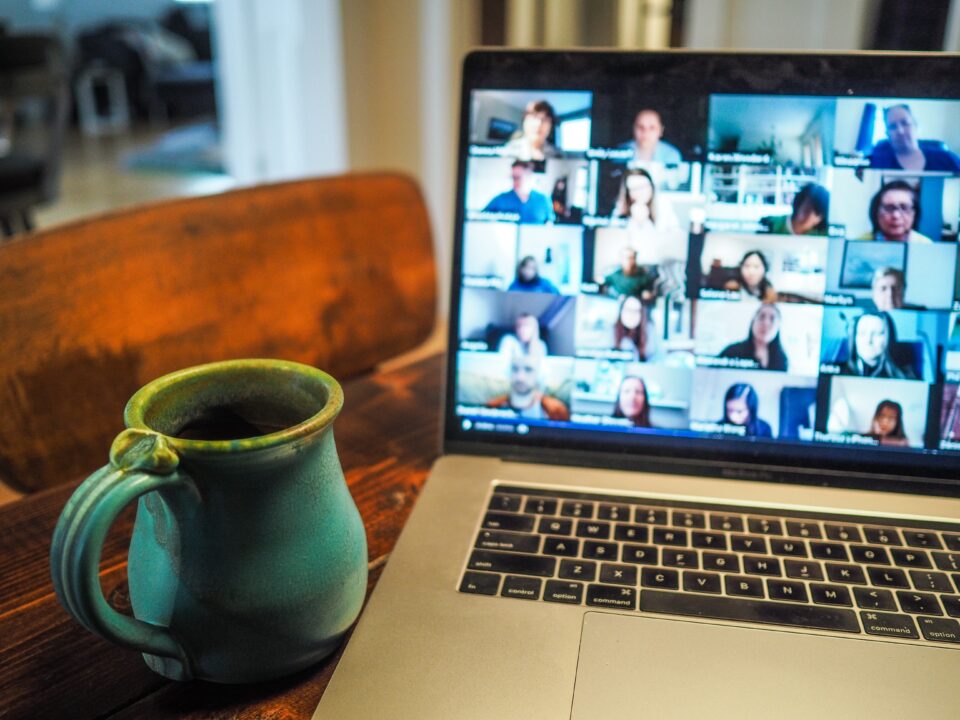 A coffee mug next to a laptop showing a Zoom session with many people.