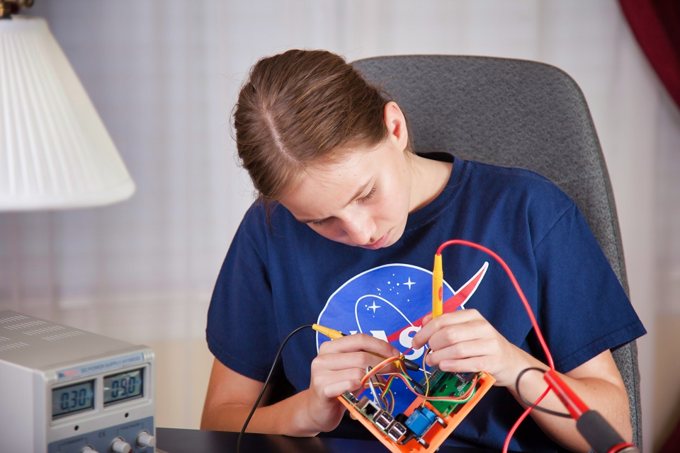 student in blue NASA tshirt working with wires for a project