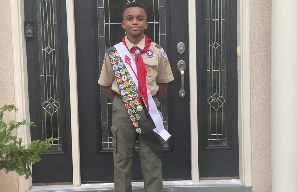 Hill Holmes standing in front of a door in his Boy Scout uniform, displaying many badges