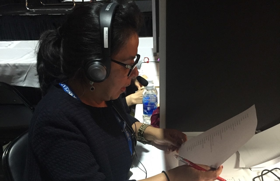 Edna Santizo references a sheet of paper, while wearing a headset and translating in the booth at ISEF