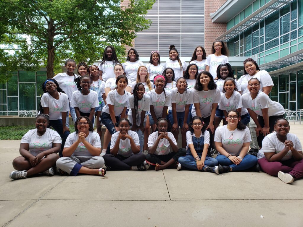 A group of girls wearing white t-shirts pose for a photograph.