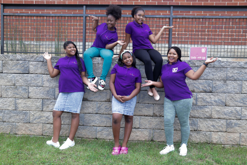 Five girls who participate in 3D Girls, Inc. pose in front of a brick wall.