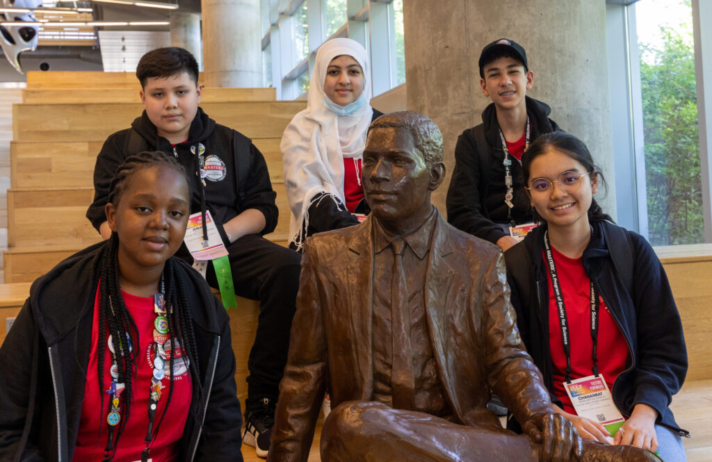 A group of 2022 Broadcom MASTERS International delegates poses for a photo with a statue in Atlanta, Georgia