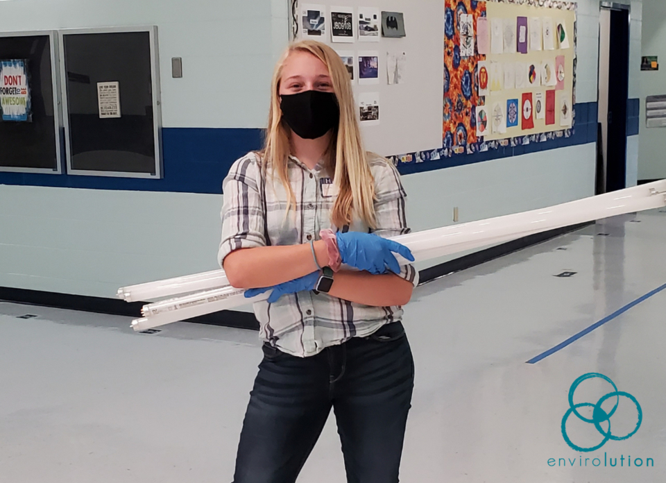 A masked volunteer holds three fluorescent lights