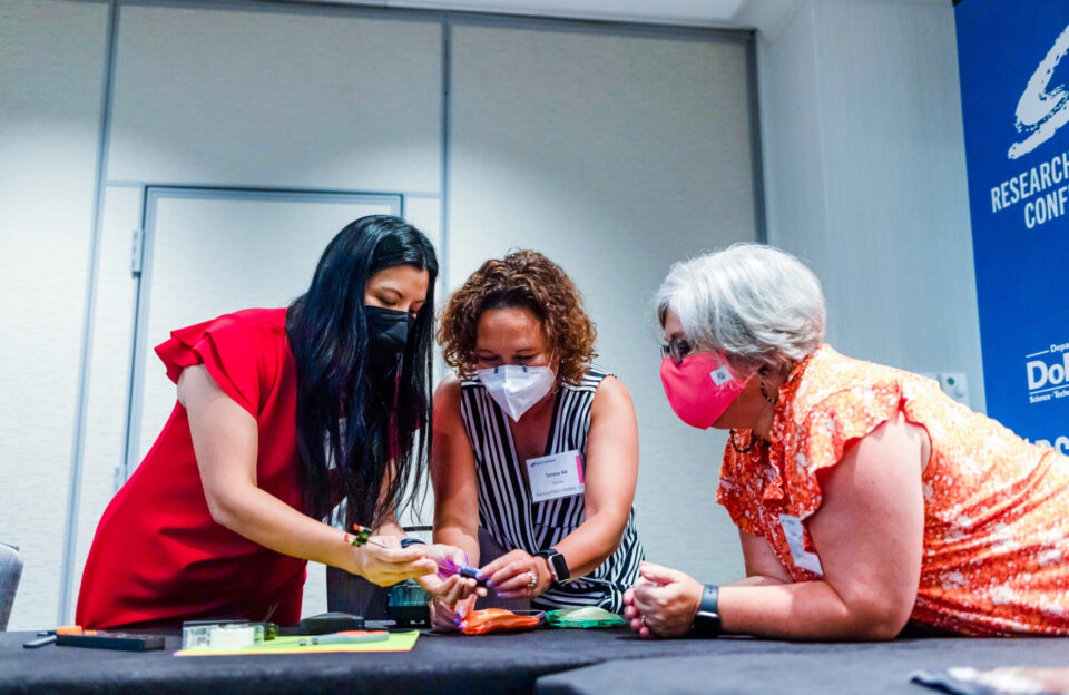 Three teachers work together on a model airplane project at the 2022 Middle School Research Teachers Conference.