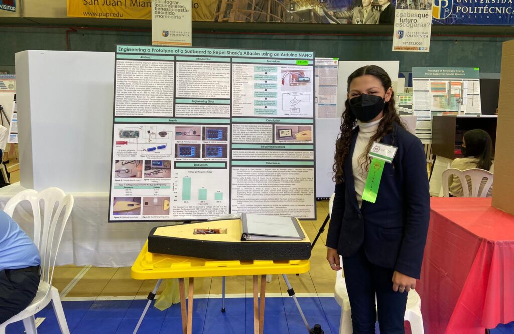 Dalismar Marrero stands in front of her project board which displays her research and prototype of a shark repelling surfboard.