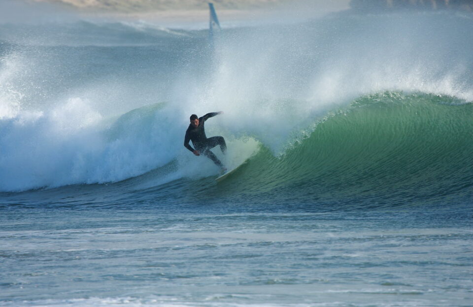 A surfer catches a wave on a lightly colored surfboard while wearing a wet suit.