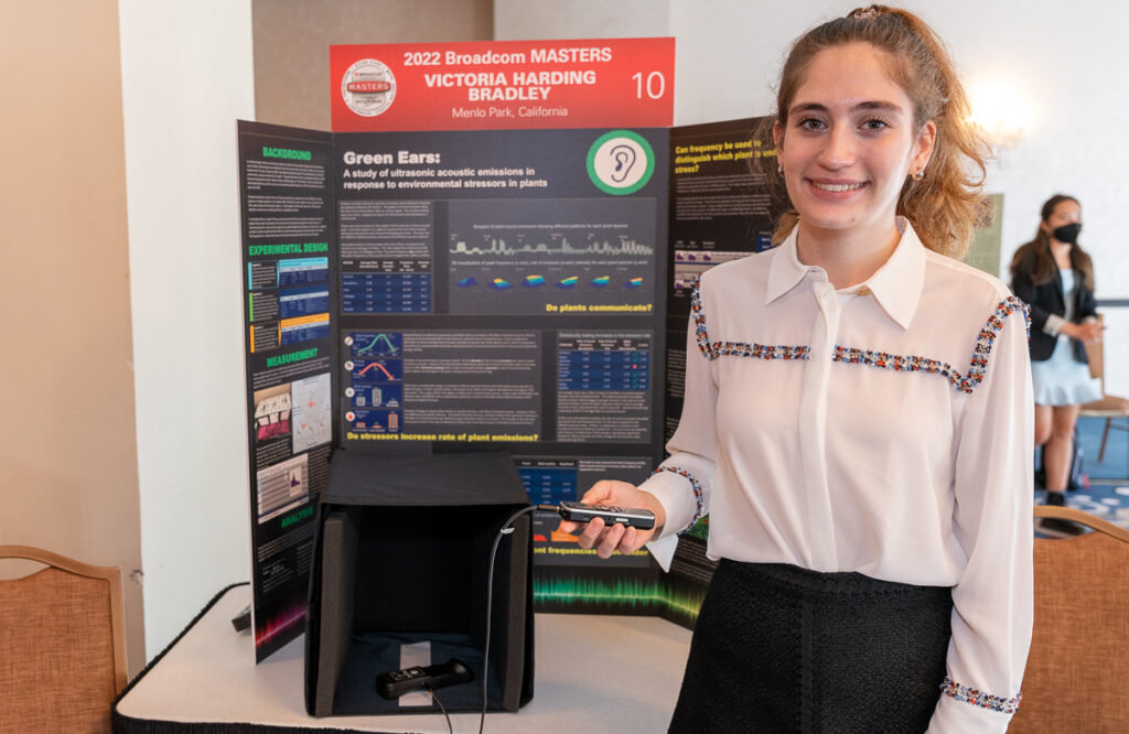 2022 Broadcom MASTERS Finalist Victoria Harding Bradley smiles in front of her project board, displaying her study of ultrasonic acoustic emissions in response to environmental stressors in plants.