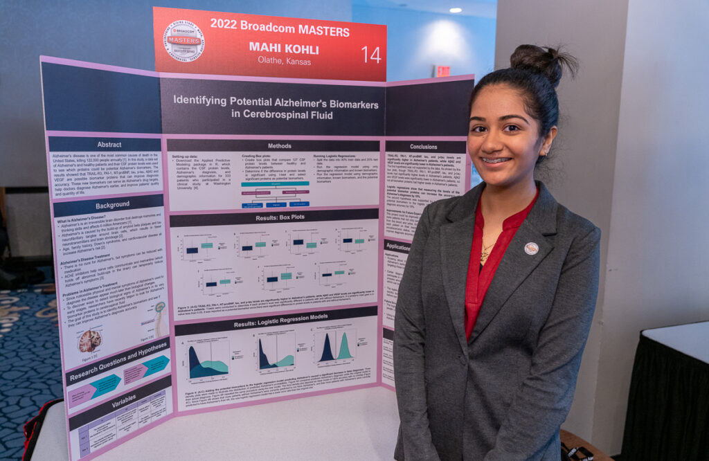 2022 Broadcom MASTERS Finalist Mahi Kohli smiles in front of her project board displaying her research on identifying potential Alheimer's biomarkers in cerebrospinal fluid.