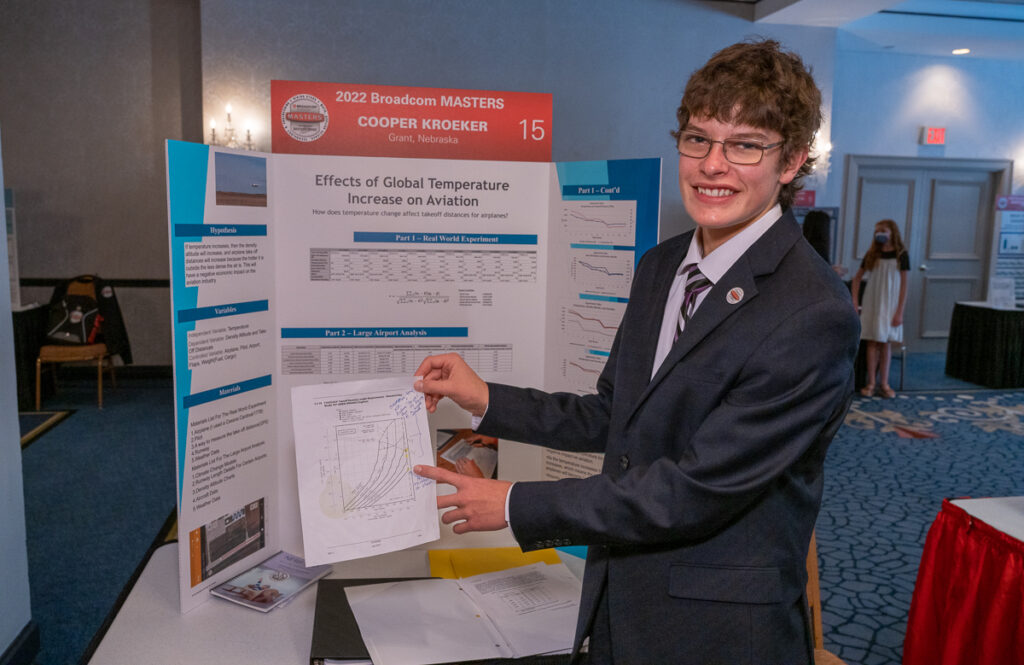 2022 Broadcom MASTERS Finalist, Cooper Kroeker smiles in front of his project board, displaying his research on the effects of global temperature increase on aviation.