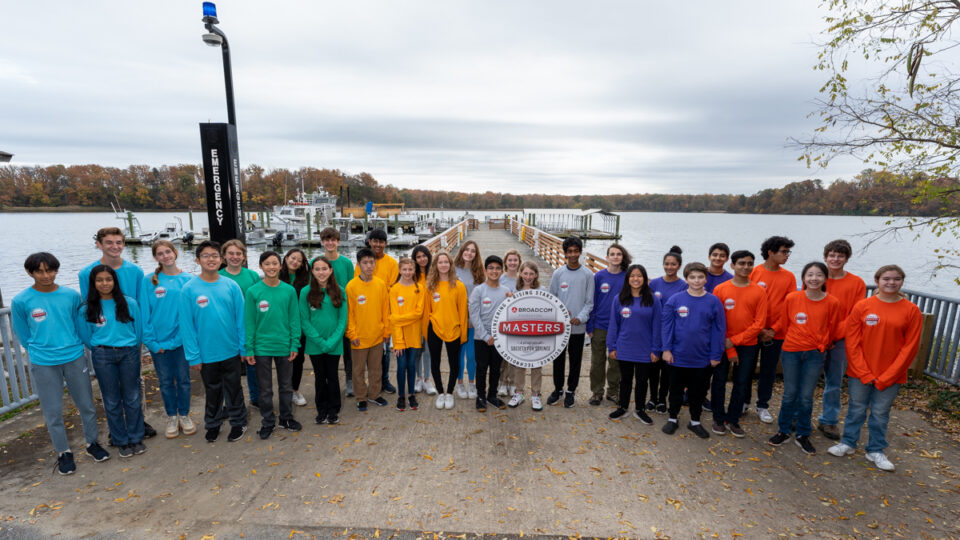 All thirty finalists, wearing their team colors, pose for a photo on a dock, with the Chesapeake Bay in the background