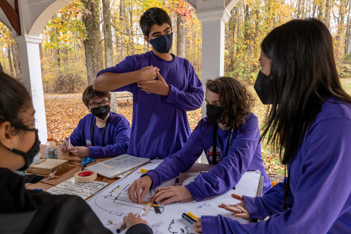 The purple team gathers around a table designing their hydraulic arm prototype