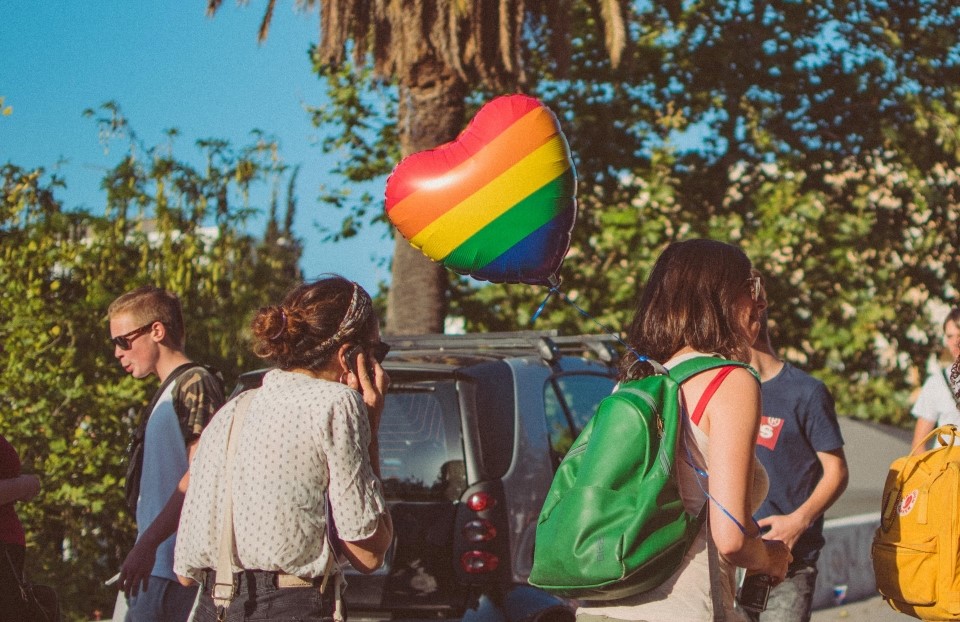 A person on the street carries a heart-shaped balloon with a rainbow pattern.