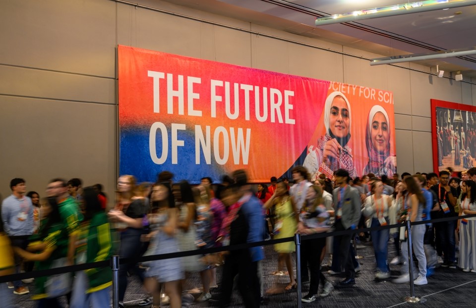 Regeneron ISEF attendees standing in line in front of a large banner that reads, "The Future of Now."