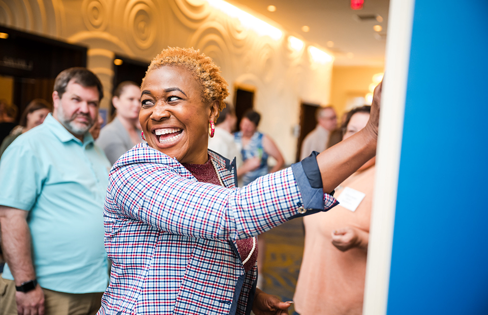 A teacher, smiling, is putting a post-it note on a chart at the Middle School Research Teachers Conference.