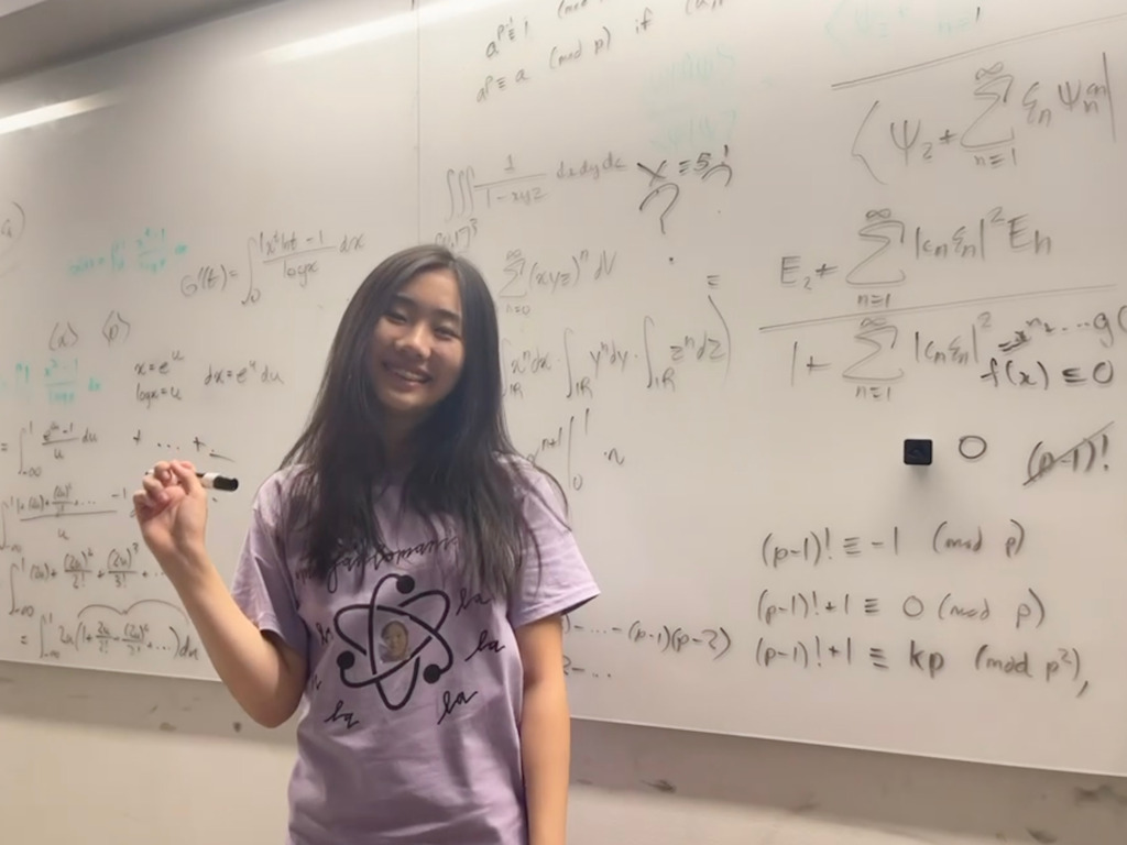 Sophie stands in front of a large whiteboard covered end to end in math equations.