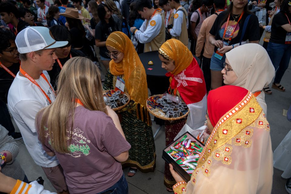 2024 ISEF - Finalists in colorful outfits exchange pins with one another.