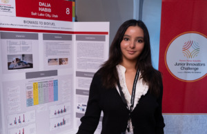 Thermo Fisher JIC finalist in front of poster board. Finalist is wearing a black sweater with a white shirt and lanyard.