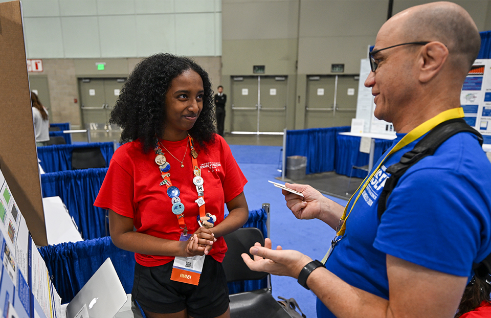 ISEF 2024 Los Angeles, CA - International Science and Engineering Fair - Display and Safety Volunteer talking with finalist about their project in the exhibit hall.