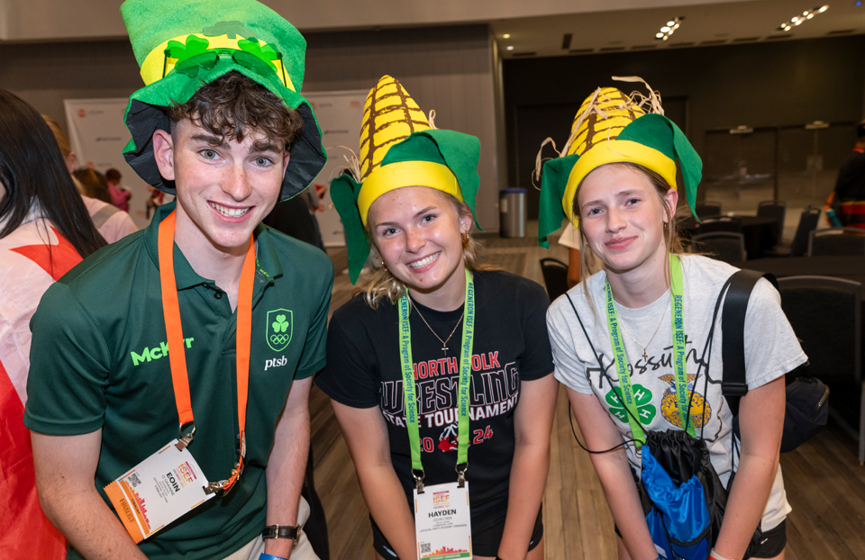 Three finalists posed for a photo while the one of the left is wearing a green leprechaun hat and the two others to the right are wearing corn hats.