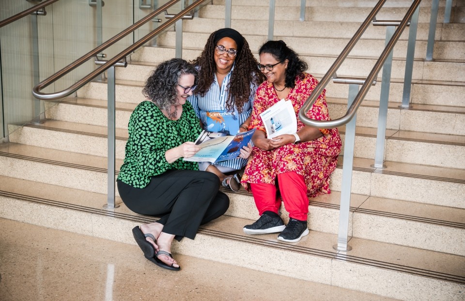 Three educators gather together in front a staircase reading Science News together