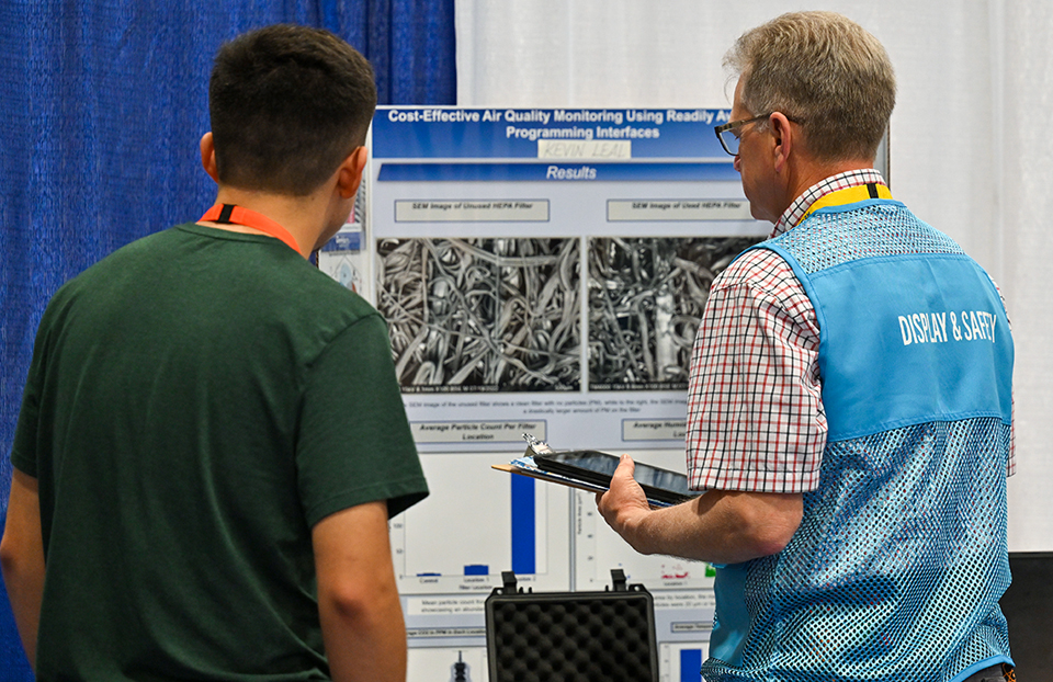 ISEF 2023 Dallas TX International Science and Engineering Fair - Display and Safety Volunteer talking with finalist about their project in the exhibit hall.