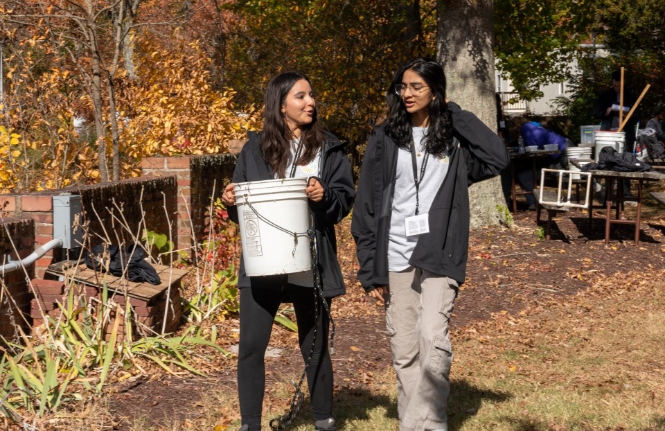 Two members of the silver team walking side by side, carrying a bucket.