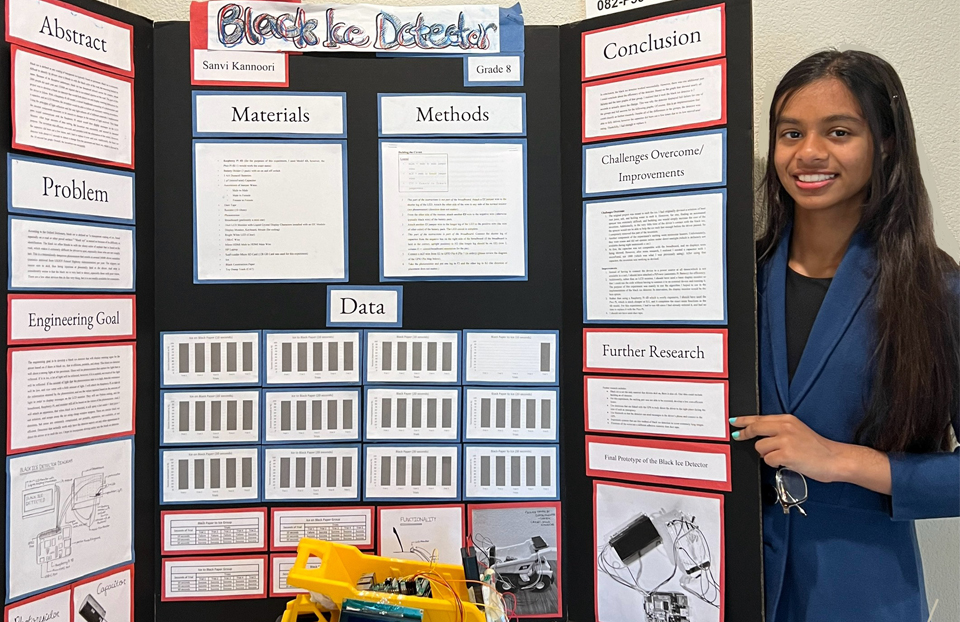 Sanvi Kannoori posing in front of her science fair project board.