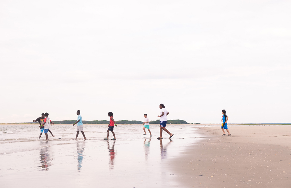 A group from the Coastal Expeditions organization are walking and playing along the shore of a beach. The sky is grey and casting over the people in the shot.