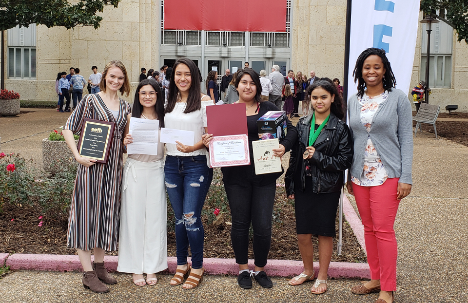 Two teachers on are on the side of their students outside the University of Houston. Posing with their accolades that they had won at the Science and Engineering Fair Houston.