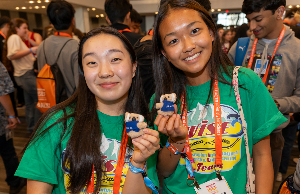 Two ISEF finalists are holding up an Australian pin that's a Koala. The finalists are wearing green shirts with orange lanyards.