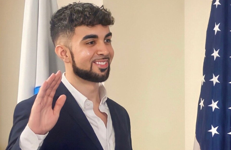 STS alumni with his right hand raised is swearing in next to the American Flag.