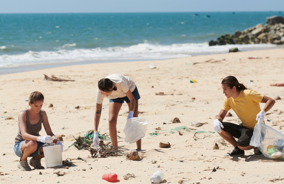 Group of volunteers picking up plastic on sandy beach.