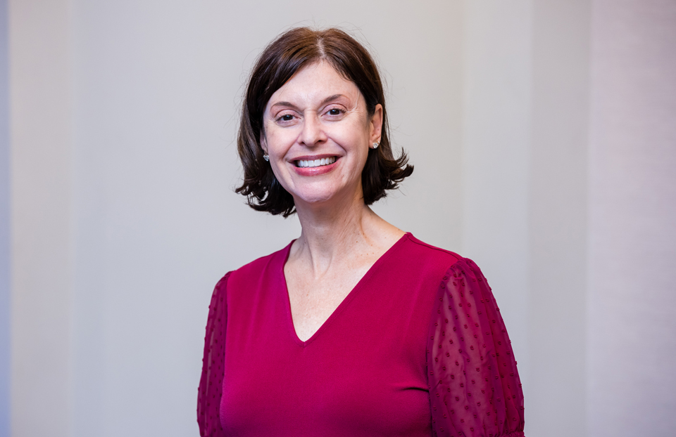 Woman with a red top and short brown hair smiling for a photo. 