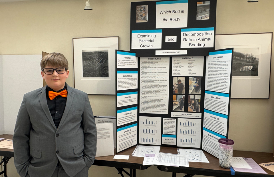A young male is wearing a red tie and posing next to his project board.