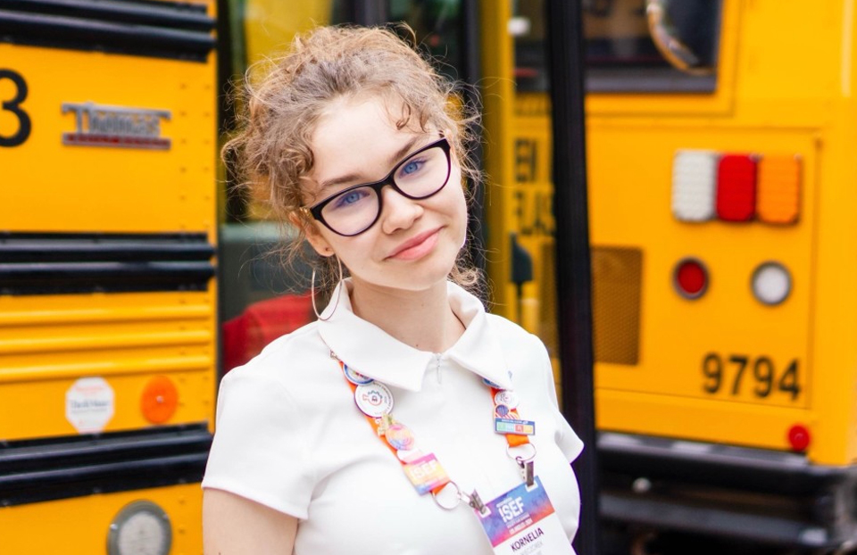 Kornelia Wieczorek at 2024 ISEF in Los Angeles - Girl with glasses and a white shirt is posing in front of yellow school buses.